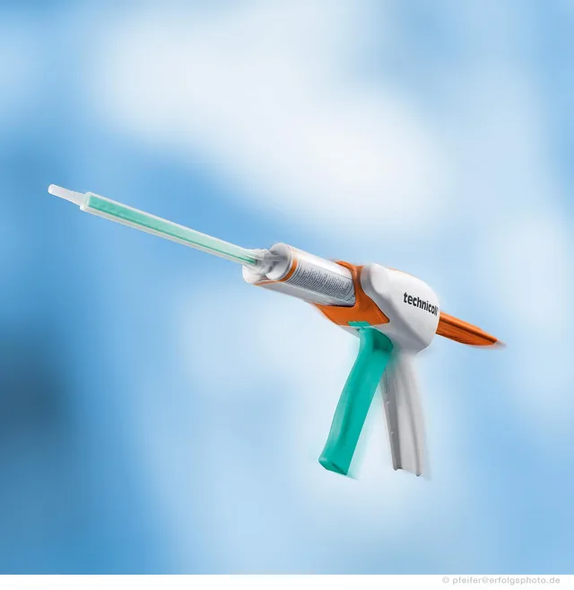 Die Klebepistole hebt sich mit Metallspitze und farbigem Griff vom blauen Hintergrund ab.