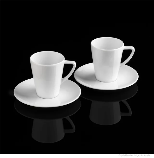 Weiße Espressotassen mit Untertellern stehen im klaren Kontrast zum schwarzen Hintergrund.